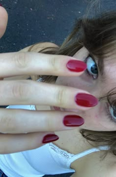 a woman with red nail polish holding her hand up to her face and looking at the camera