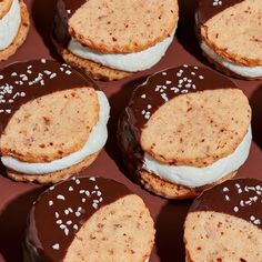 chocolate covered cookies with white frosting and sprinkles are arranged on a red surface