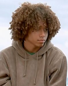 a young man with curly hair wearing a brown hoodie and looking off to the side