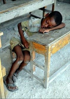 a young boy sitting on top of a wooden bench next to a table and chairs