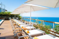 an outdoor dining area overlooking the ocean with white umbrellas and sun loungers set up