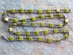 a green and silver chain with square beads on it's end, sitting on a rock