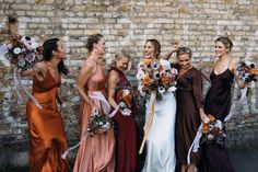 a group of women standing next to each other near a brick wall holding bouquets