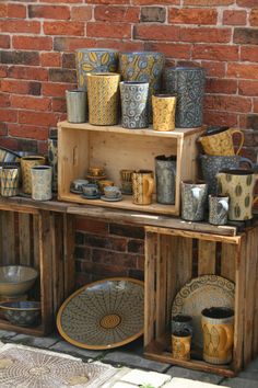 a wooden table topped with lots of vases and bowls next to a brick wall