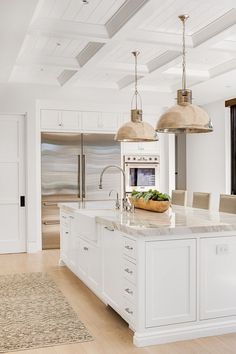 a large kitchen with white cabinets and an island in the middle is decorated with pendant lights