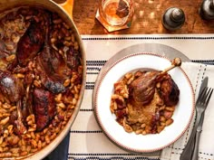 a large pot filled with meat and beans on top of a table next to a glass of wine