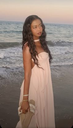 a woman standing on top of a beach next to the ocean with her hand in her pocket