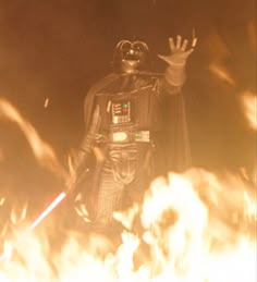 a man dressed as darth vader is standing in front of fire with his hands up