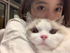 a woman is holding a white cat in her arms while she looks at the camera