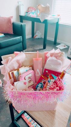 a pink basket filled with lots of items on top of a wooden table next to a couch