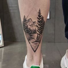 a man's foot with a mountain and trees tattoo on the side of his leg