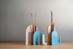 two toothbrush holders with toothbrushes in them on a wooden table next to a gray wall