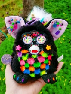 a hand holding a small stuffed animal with multicolored decorations on it's face