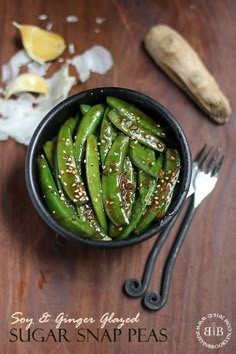 a bowl filled with green beans on top of a wooden table next to utensils