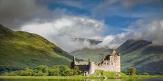 a castle sitting on top of a lush green hillside next to a body of water