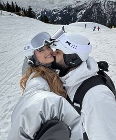 a man and woman kissing in the snow with skis on their heads as they stand close to each other