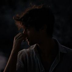 a young man is talking on his cell phone in the dark, while looking off into the distance