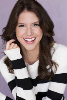 a smiling woman with long brown hair and black and white striped sweater is posing for the camera