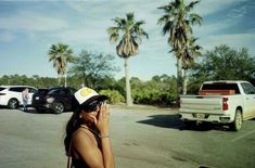 a woman talking on her cell phone while standing in a parking lot with palm trees