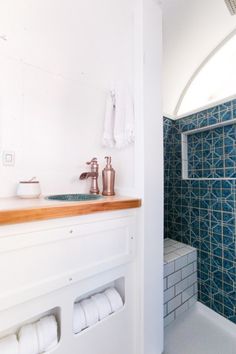 a bathroom with blue tiles on the walls and wood countertop, along with a copper faucet