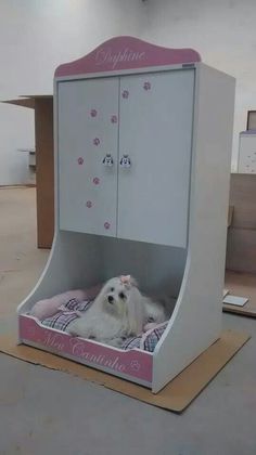 a small white dog laying in a pink and white pet bed that is shaped like a wardrobe