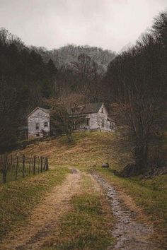 an old house sitting on top of a lush green hillside next to a dirt road