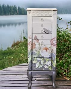 a painted cabinet sitting on top of a wooden table next to a body of water