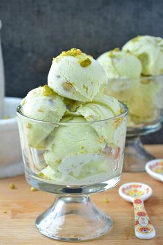 three scoops of ice cream sitting in a glass bowl on a wooden table next to two spoons