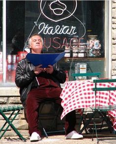 a man sitting in front of a restaurant reading a menu while holding a clipboard