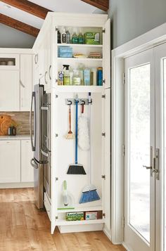 an organized kitchen with white cabinets and wood floors, including brooms and mop's