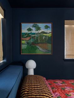 a bedroom with blue walls and a painting on the wall next to a bed that has a colorful bedspread