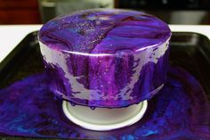 a purple and white cake sitting on top of a black tray next to a cup