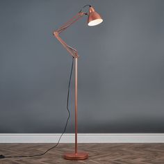 a floor lamp with a wooden base and an orange shade on the top, against a gray wall