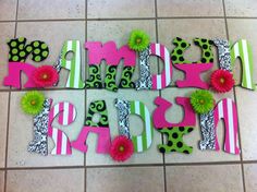 the letters are decorated with pink, green and black paper flowers on a tile floor