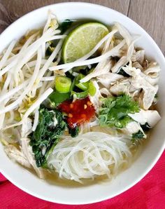 a white bowl filled with noodle and chicken soup on top of a red cloth