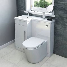 a white toilet sitting next to a sink and mirror in a bathroom under a window