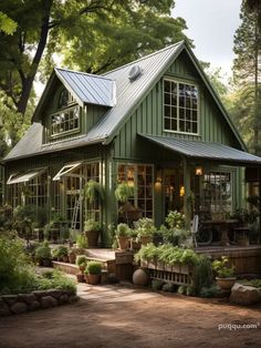 a green house with lots of windows and potted plants on the front porch, surrounded by greenery