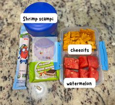 some food is sitting in a container on the counter next to a blue bowl with cheeses, watermelon and shrimp scamp