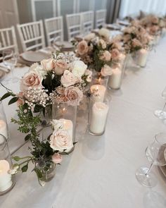 a long table with candles and vases filled with flowers on top of white clothed tables