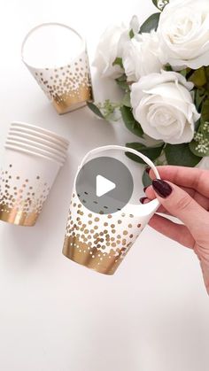 a hand holding a cup with gold dots on it and white roses in the background