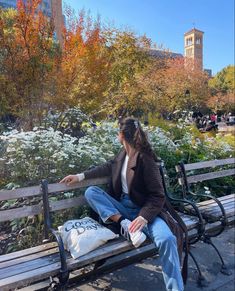 a woman is sitting on a bench in the middle of a park with flowers and trees