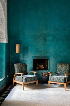 two chairs and a table in front of a blue wall with a fire place on it