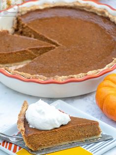 a slice of pie on a plate with whipped cream and pumpkins in the background