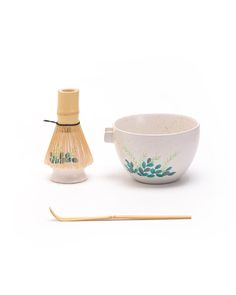 a white bowl next to a bamboo stick and an empty cup with green leaves on it