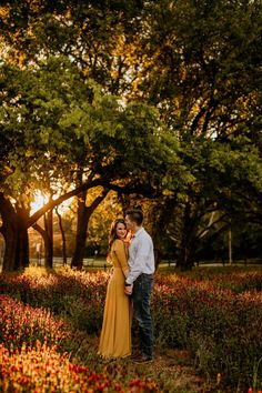 a man and woman standing in the middle of a field with red flowers at sunset