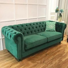 a green couch sitting on top of a hard wood floor next to a white wall