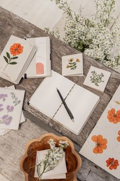 notebooks and flowers on a wooden table next to a bowl with watercolor paper