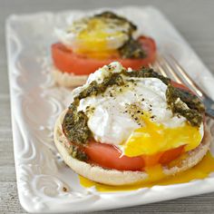 an egg and tomato sandwich is on a plate with a fork next to the burger