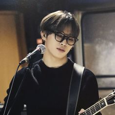 a young man with glasses playing an acoustic guitar in front of a microphone and sound board