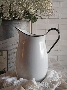 a white pitcher sitting on top of a table next to a vase filled with flowers